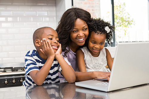 Mother and children using laptop in the kitchen