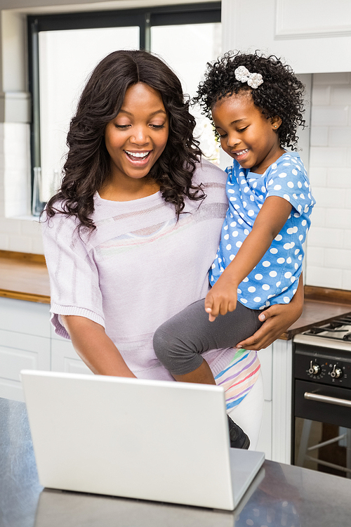 Mother using laptop while carrying kid in kitchen