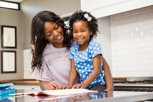 Young girl doing her homework with her mother in the kitchen