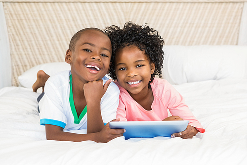 Happy siblings using tablet on bed at home