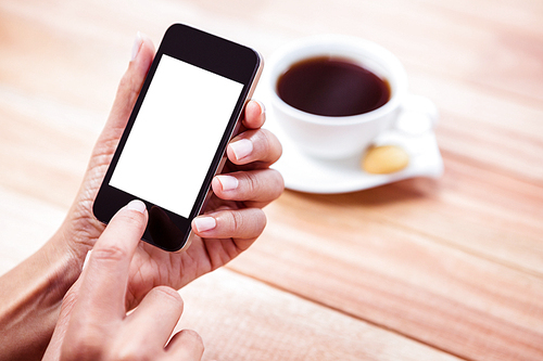 Overhead of feminine hands using smartphone with coffee and biscuit on table