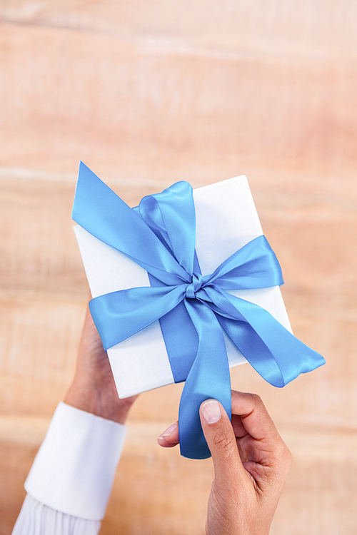 Woman presenting gift with blue ribbon on desk