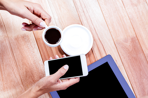 Businesswoman holding smartphone and coffee cup at work