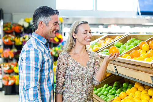 Smiling couple holding an orange in grocery shop