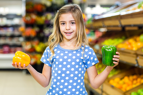 Smiling girl holding two pepper at supermarket