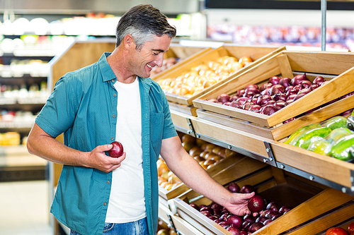 Smiling man choosing a onion at supermarket