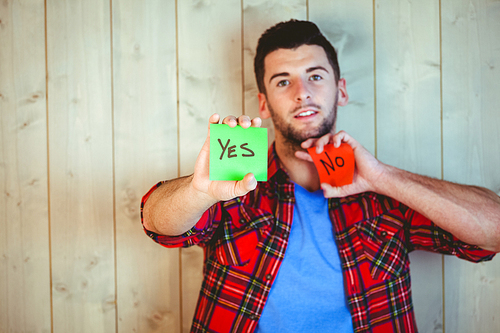 Handsome hipster showing yes and no cards against wooden background