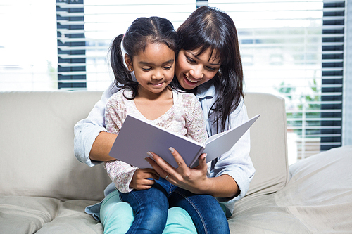 Happy mother reading book with her daughter in living room
