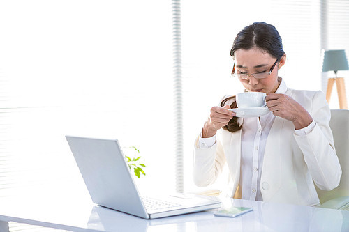 Businesswoman drinking coffee behind her computer at the desk in work