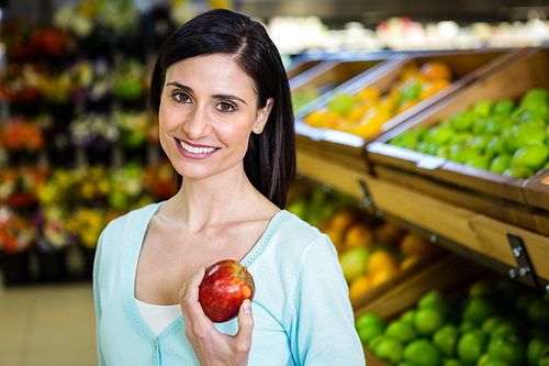 Portrait of a smiling woman picking apple in supermarket