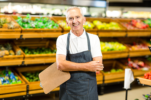 Mature worker with arms crossed and clipboard in supermarket