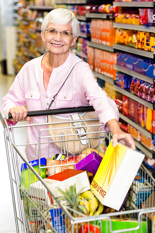 Smiling senior woman taking corn flakes box in supermarket