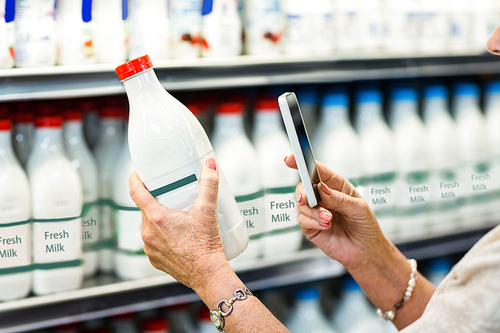 Close up of senior woman taking picture of milk bottle at the supermarket