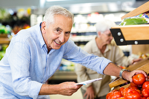 Smiling senior man with list buying apple at grocery shop