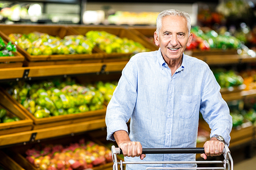 Smiling senior man holding trolley in supermarket