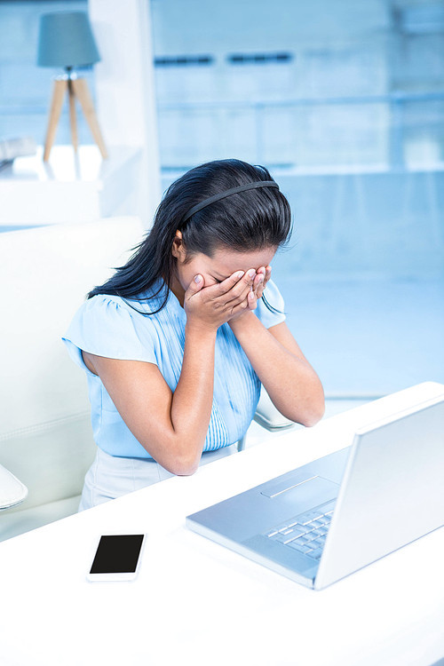 Worried businesswoman covering her face at her desk