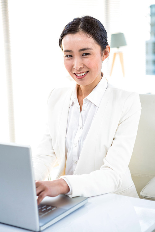 Smiling businesswoman using laptop at her desk