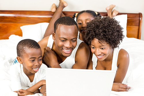 Happy family lying on the bed with laptop