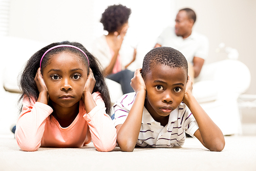 Unhappy kids sitting on the floor beside arguing parents