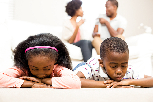 Unhappy kids lying on the floor beside arguing parents