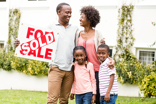 Happy family standing together while holding a sold sign