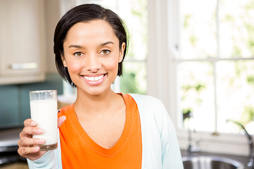 Happy brunette holding glass of milk in the kitchen