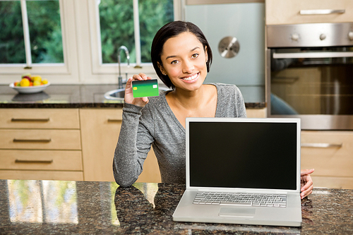 Smiling brunette showing laptop and credit card in the kitchen
