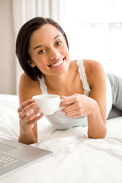 Smiling brunette holding cup on the bed