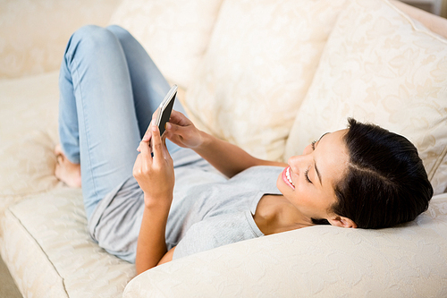 Smiling brunette using smartphone on the sofa