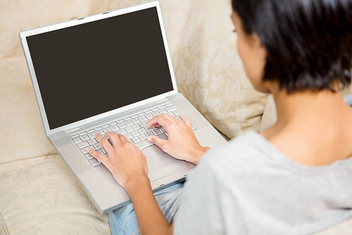 Over shoulder view of brunette using laptop on the sofa