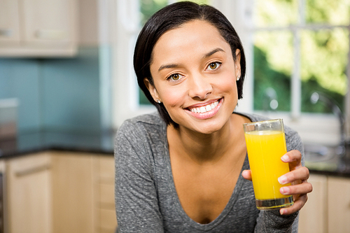 Smiling brunette holding glass of orange juice in the kitchen