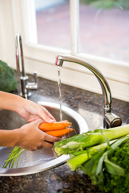 Mid section of woman washing carrots in the kitchen