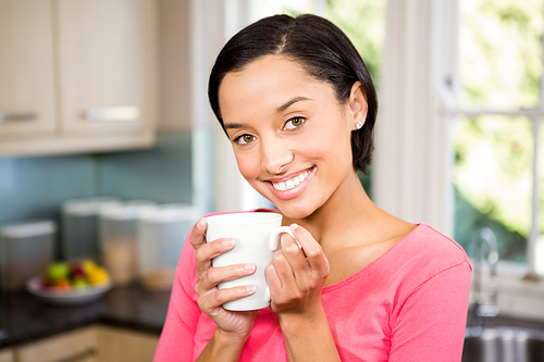Smiling brunette holding white cup in the kitchen