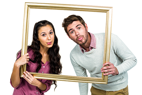 Couple sticking out tongue while holding picture frame on white background