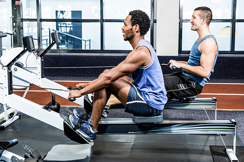 Muscular men using rowing machine at gym