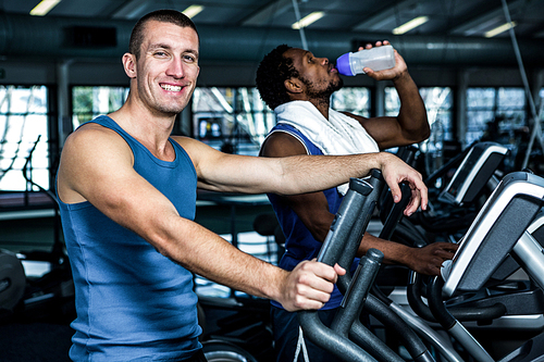 Smiling man using elliptical machine at gym