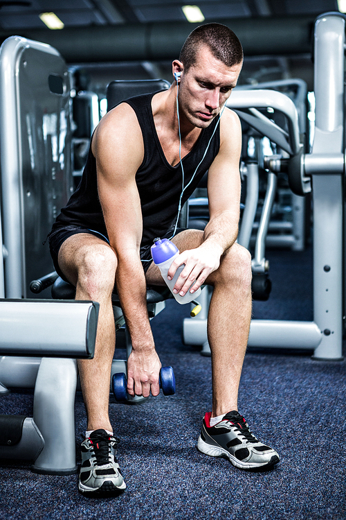 Muscular man with headphones lifting dumbbells at gym