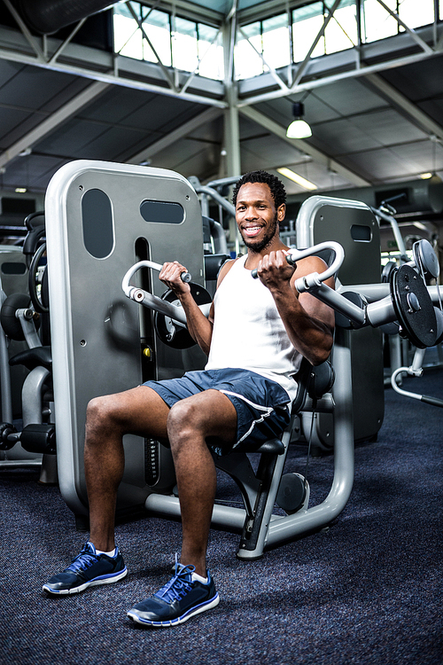 Smiling muscular man using exercise machine at gym