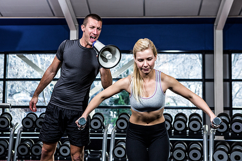 Male trainer motivating fit woman with megaphone at gym
