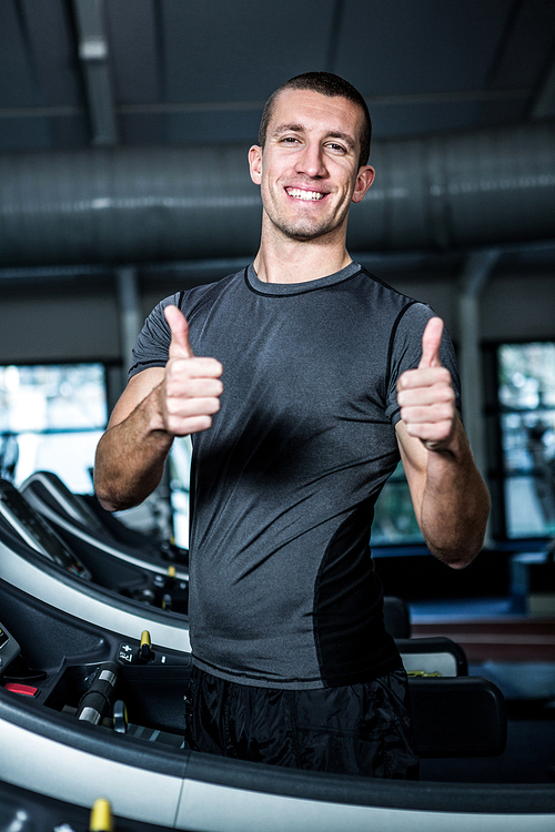 Muscular man on treadmill showing thumbs up at gym