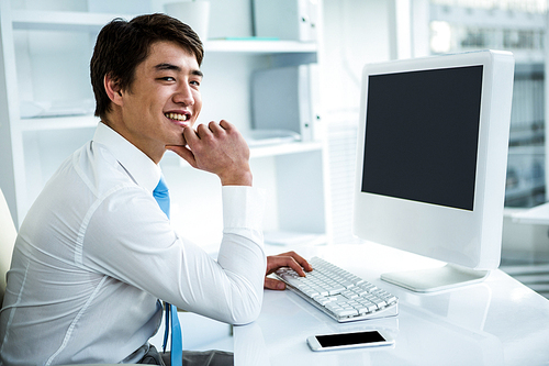 Smiling asian businessman using his computer in his office