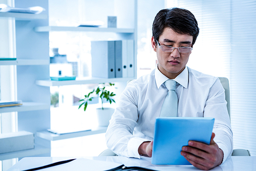 Serious asian businessman using his tablet in his office