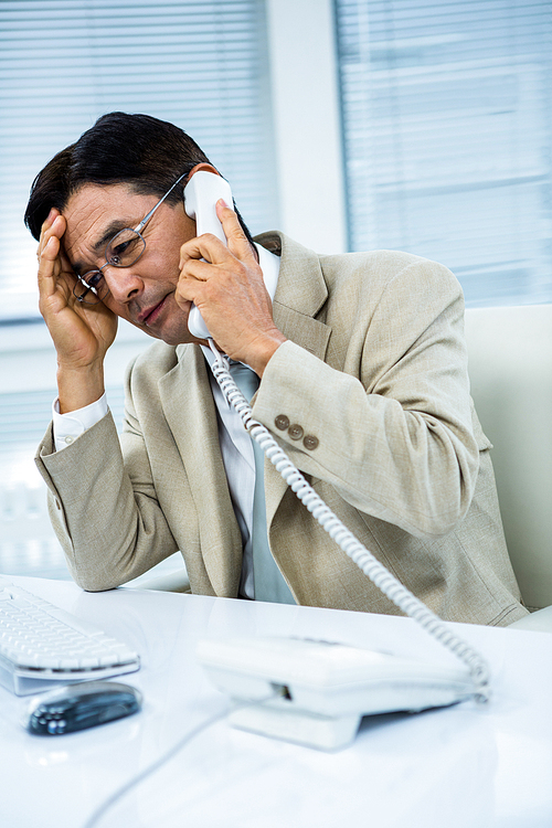 Troubled asian businessman on the phone in his desk