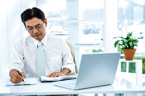 Focused asian businessman writing in office