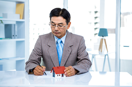 Businessman taking notes with miniature house in office
