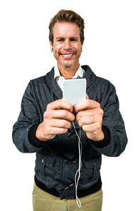 Portrait of happy man listening music while using mobile phone against white background