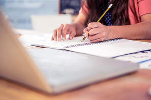 Businesswoman writing in book on desk at creative office