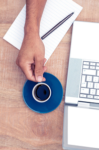 Cropped image of businessman having coffee while using laptop on desk in office