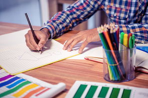 Midsection of designer drawing on book at desk in creative office