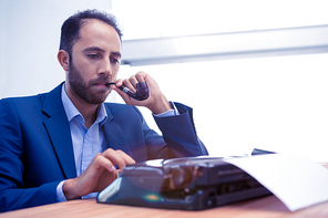 Businessman using typewriter while holding smoking pipe in creative office